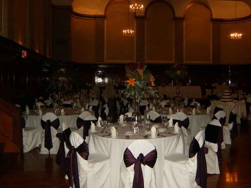 Grand Ballroom setup in maroon and white theme with chair covers, flower decor centerpieces, and white plate place settings at The Corinthian Event Center.