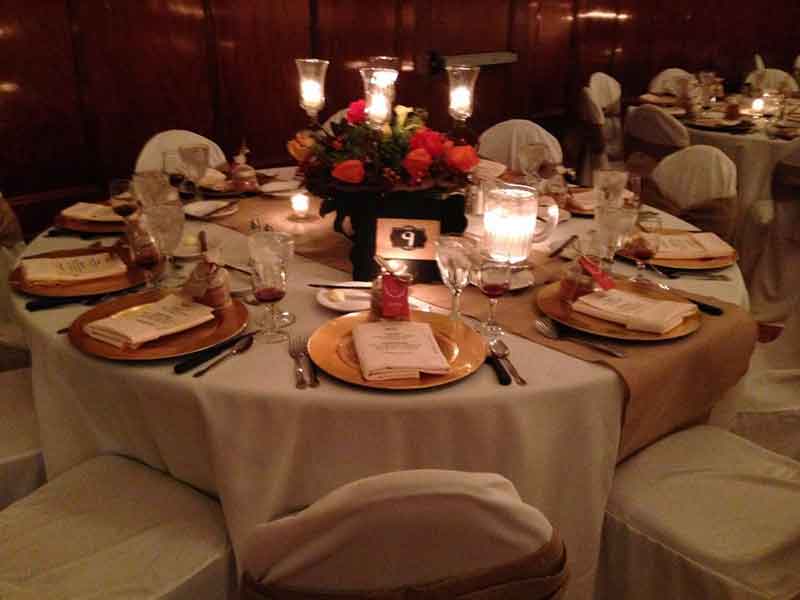 Grand Ballroom setup in gold and white theme with chair covers, flower decor centerpieces, and gold plate place settings at The Corinthian Event Center.