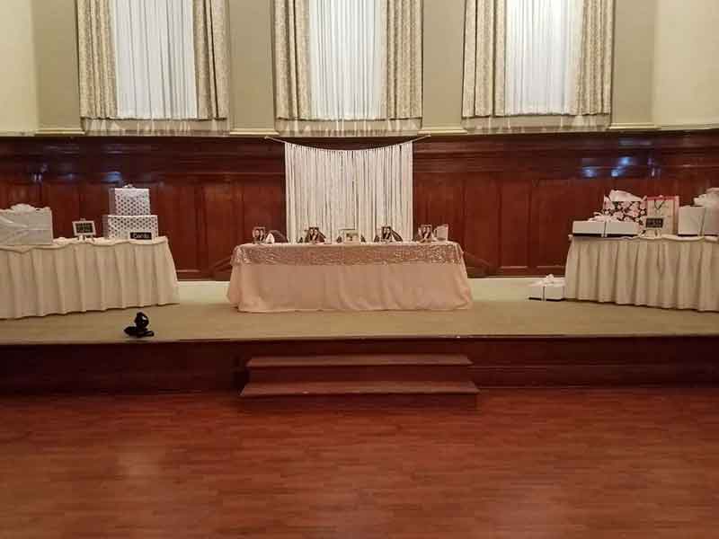 Head table and presents table setup on Grand Ballroom stage with backdrop in pink theme at The Corinthian Event Center.
